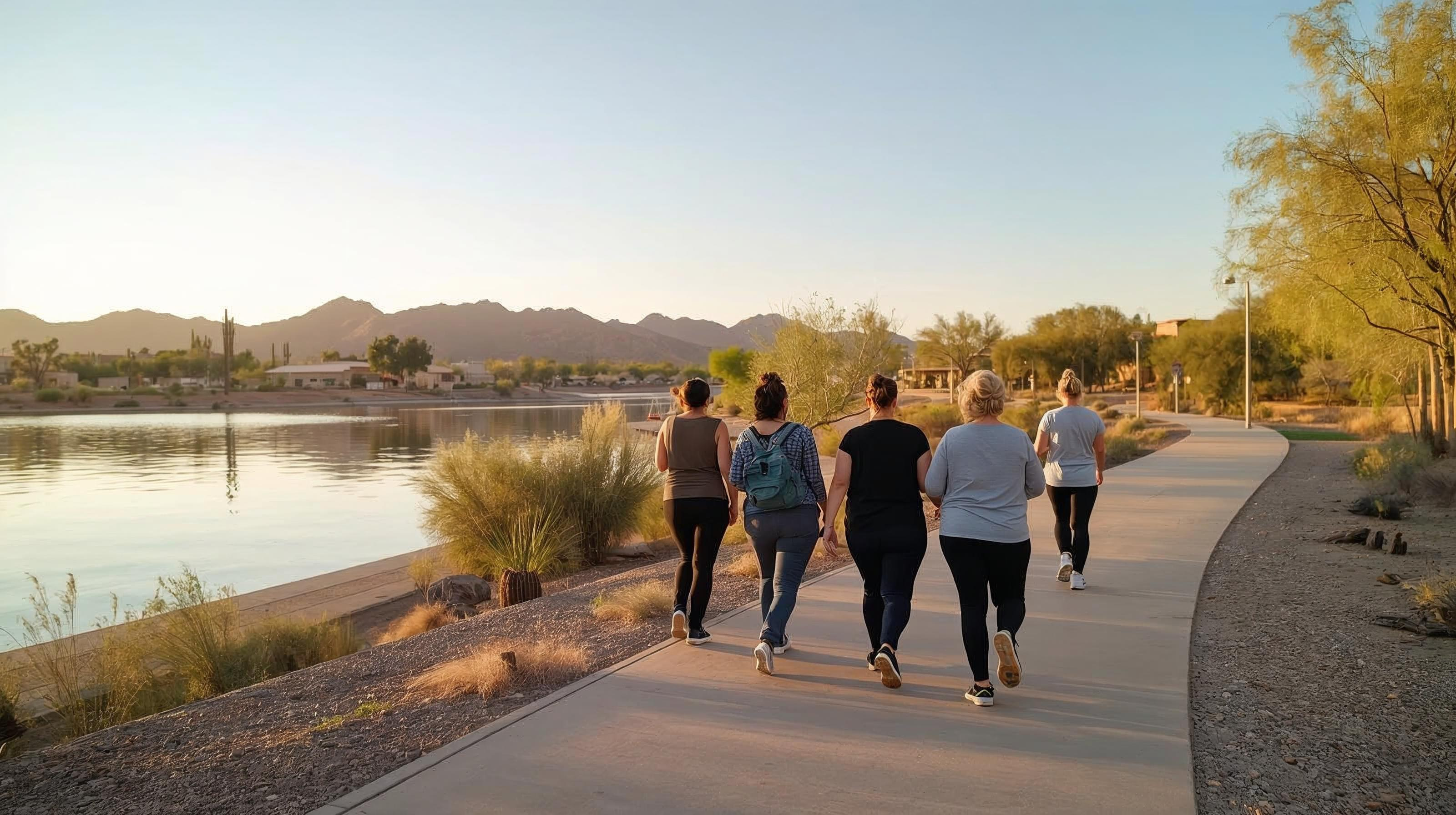 A small group of women walking together on a paved path beside a lake at sunset.